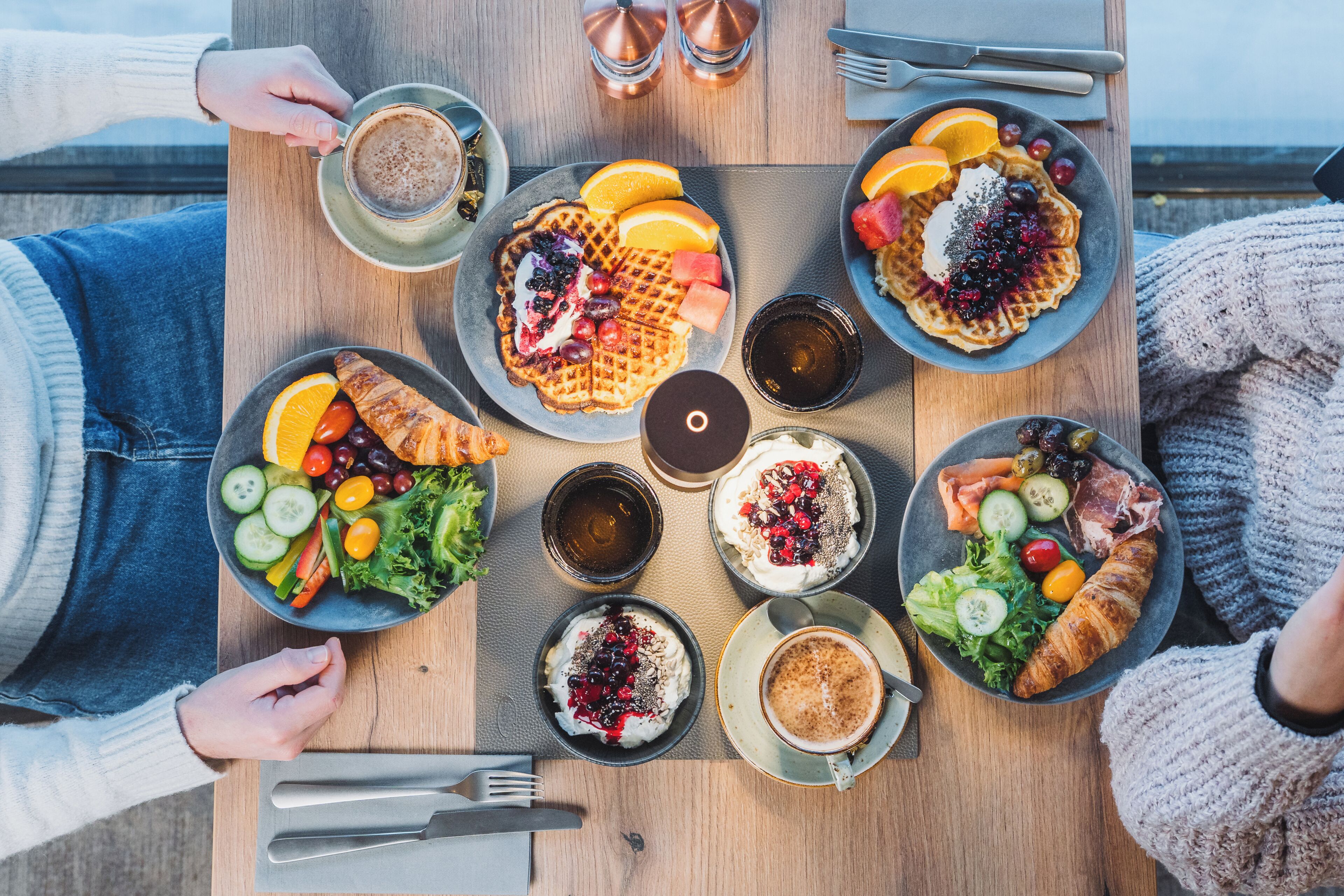 Un tavolo imbandito con diversi prodotti per la colazione, tra cui waffle, croissant e un'insalata.