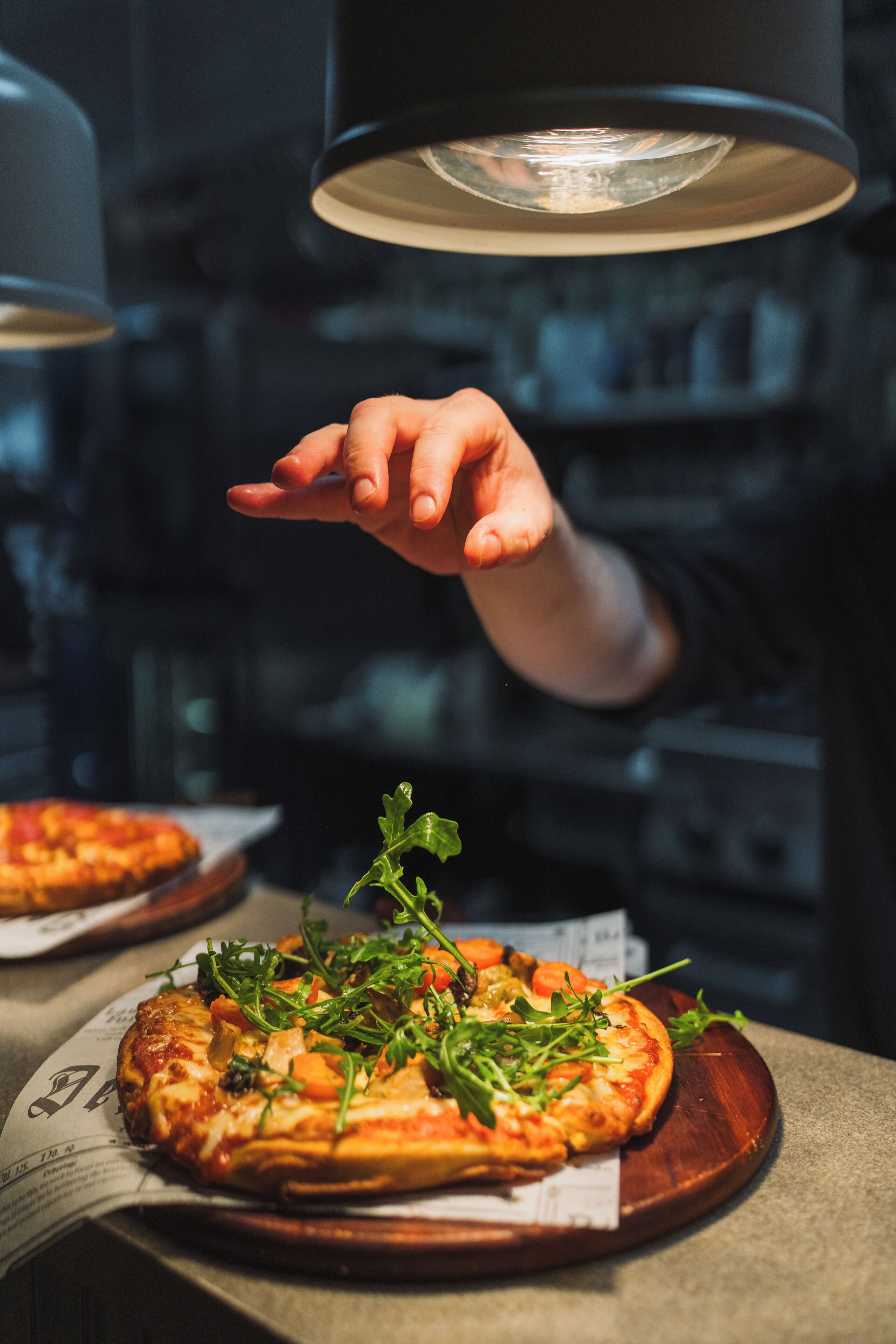 Pizza op een houten plank, met een hand die ernaar wijst.