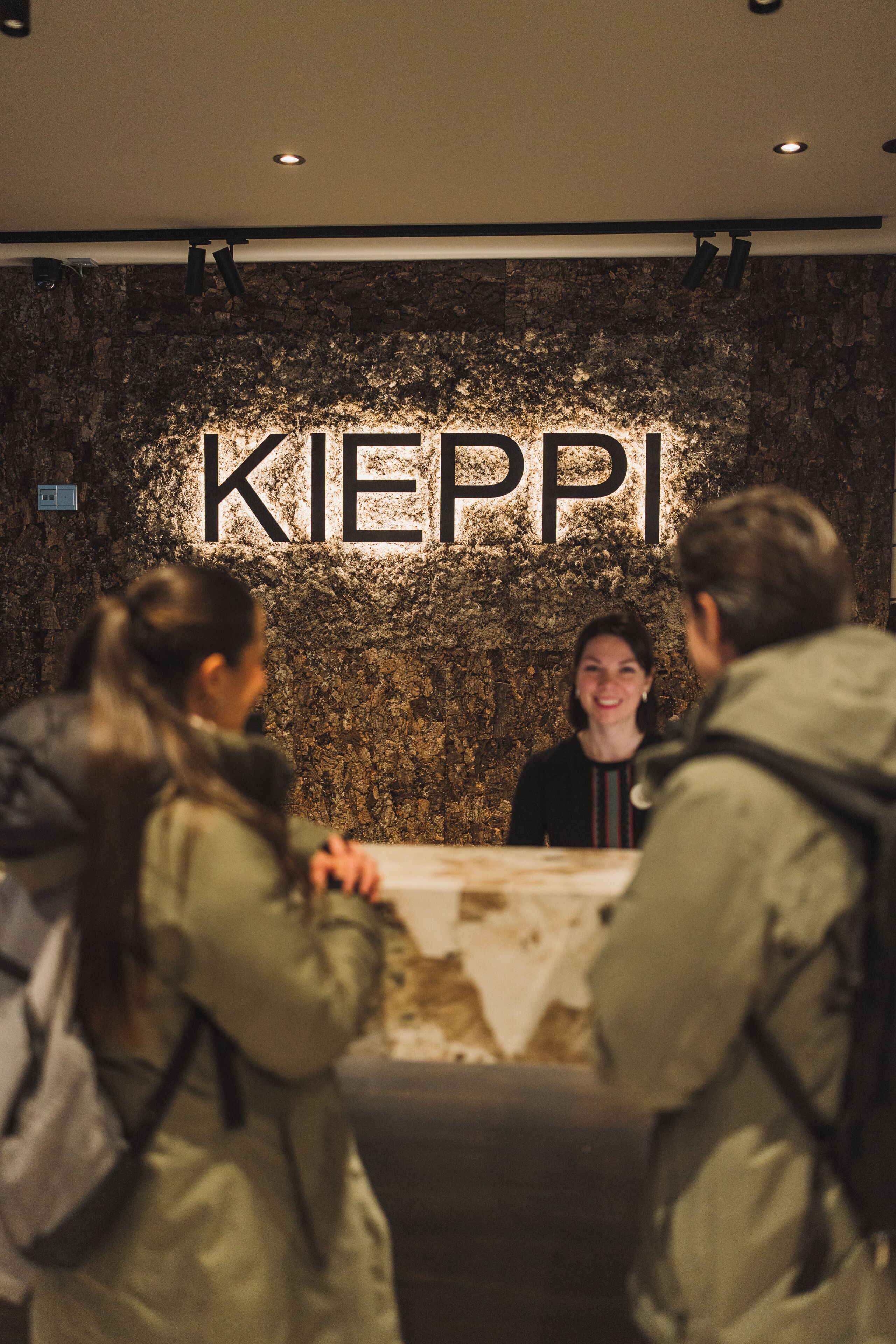 Een receptiebalie met een bord waarop 'KIEPPI' staat, voor een gestructureerde muur.