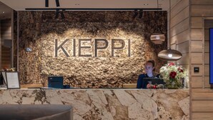 A reception desk with a stone wall background and the word 'KIEPI' prominently displayed. - Wilderness Hotel Kieppi (Saariselkä)