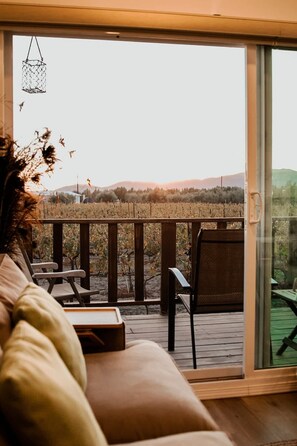 A balcony with a view of a vineyard and hills. There is a cushioned seating area with a table and chairs.