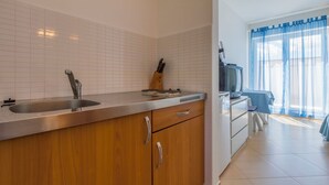 A kitchen with a stainless steel sink, wooden cabinets, and a dining area with a table and chairs. - Apartment Mirta 1 (Dramalj)
