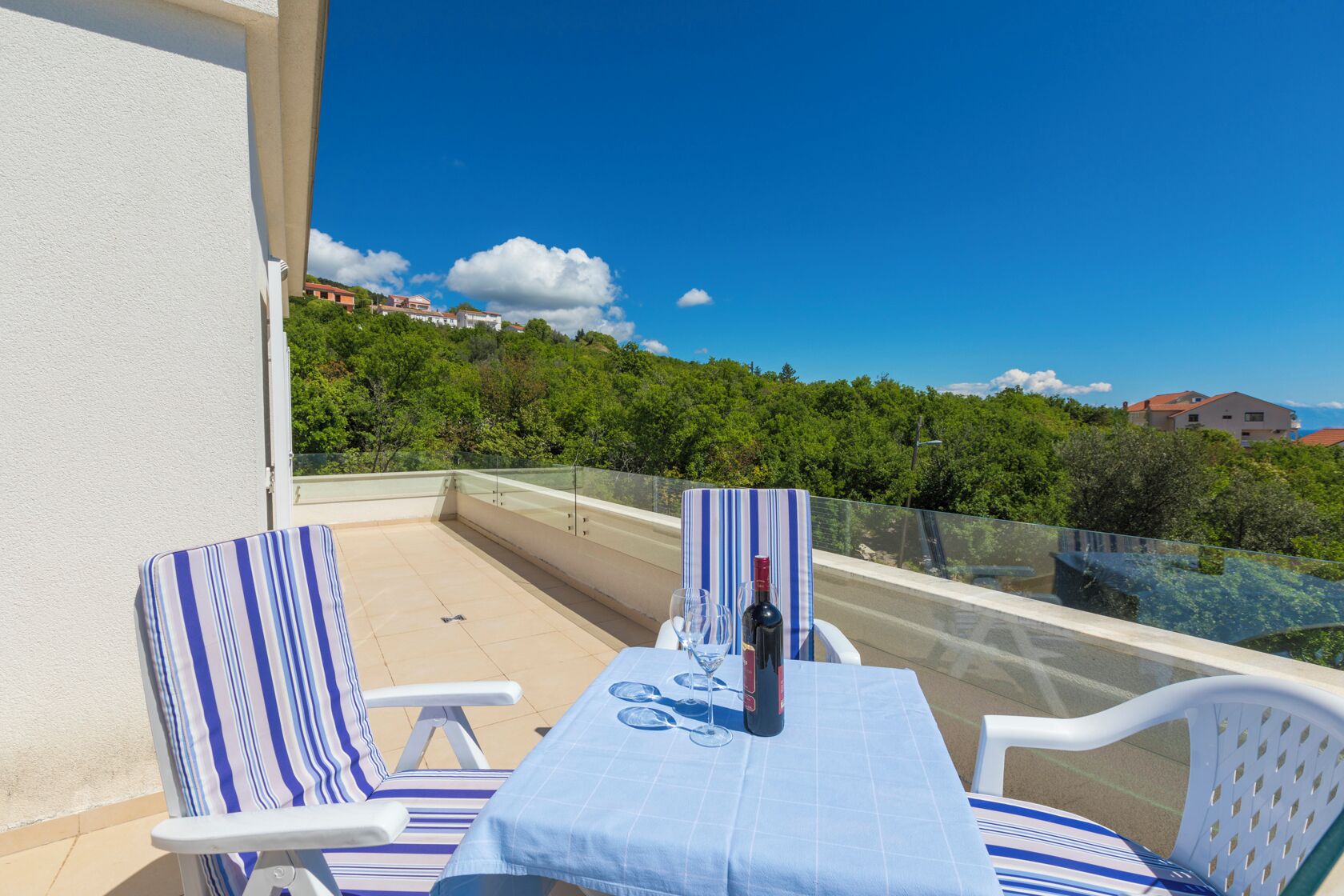 A balcony with a table set for two, two striped chairs, and a bottle of wine.
