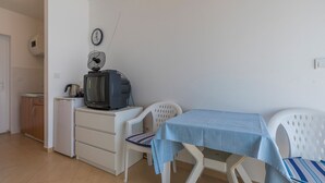 A compact kitchen with a refrigerator, a small stove, and a television on a white cabinet. There is a dining table with a blue tablecloth and two white chairs. - Apartment Mirta 1 (Dramalj)