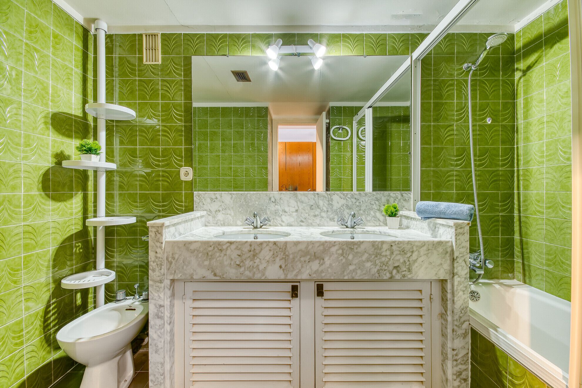 Un baño con baldosas verdes estampadas, un lavamanos blanco, un espejo y una ducha.
