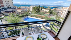 A balcony with a table set for dining, overlooking a swimming pool and a coastal cityscape.