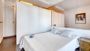 A bedroom with a large bed, a wardrobe, a mirror, and a small plant on the dresser.