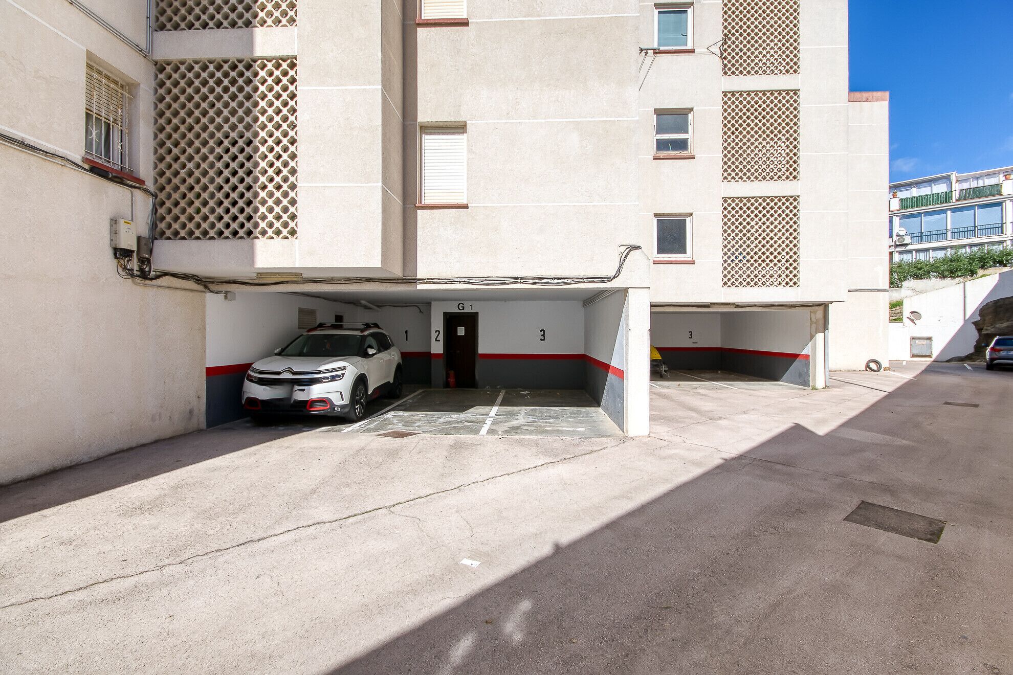 A parking garage with numbered parking spaces, a white car parked in space 1, and a building with a lattice window design.