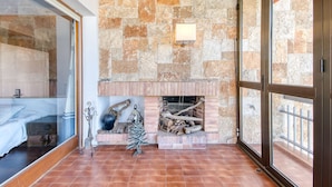 A room with a stone wall, a fireplace with logs, a metal railing, and a window.