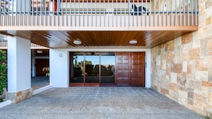 A building entrance with a stone facade, a wooden balcony, and a large glass door.