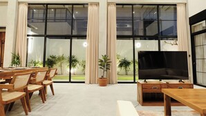 Un salón amplio con un televisor grande, muebles de madera y ventanas grandes con cortinas.