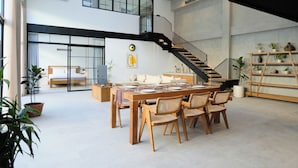 Un interior espacioso y moderno con una mesa de comedor de madera, sillas de mimbre, una escalera y una estantería con plantas.