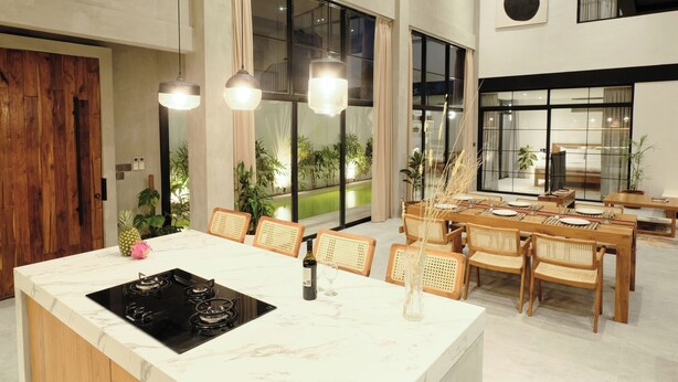 Un comedor moderno con una isla de mármol, sillas de madera e iluminación colgante.