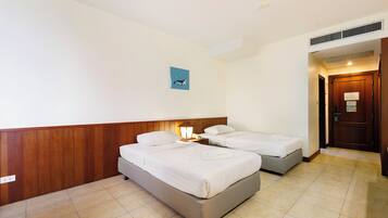 A hotel room with two single beds, a wooden headboard, a nightstand with a lamp, and a small wall art.