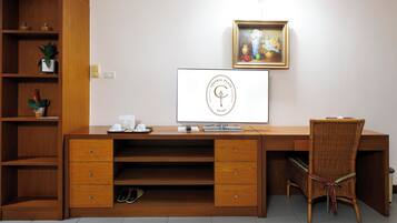 A hotel reception desk with a computer monitor, a framed logo, and a wicker chair.