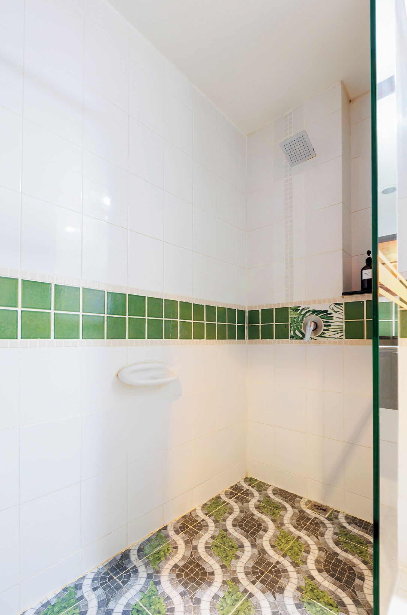 A bathroom with white tiles, a green and white tile border, and a patterned floor.
