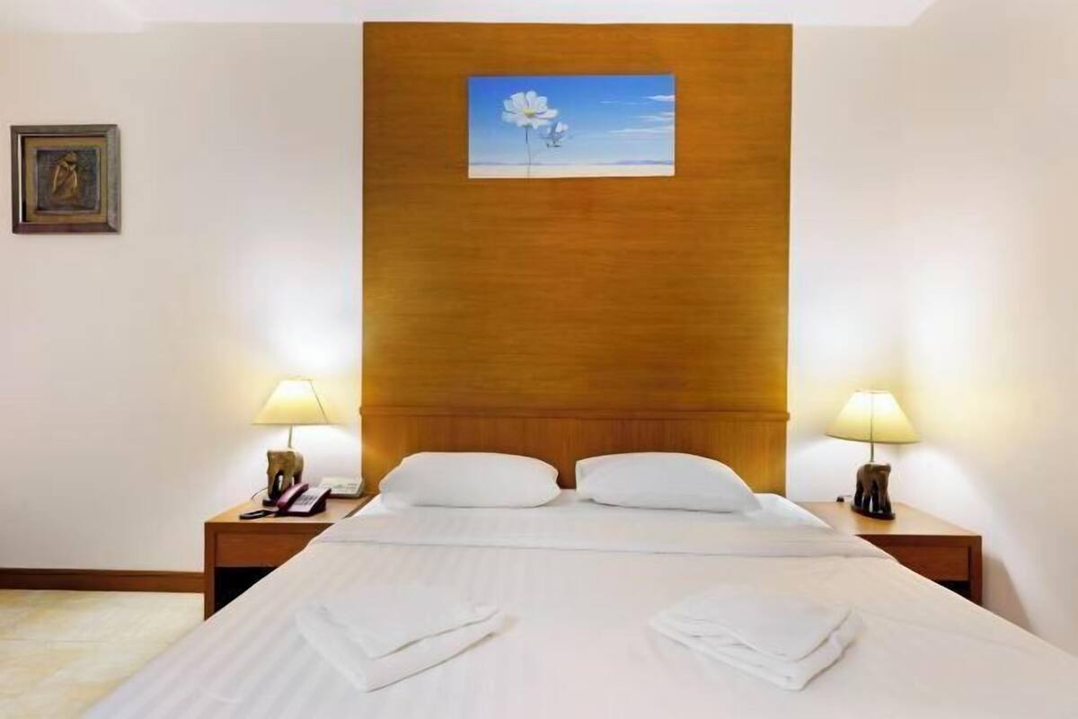 Ein Hotelzimmer mit einem großen Bett, zwei Nachttischen mit Lampen, einem gerahmten Bild an der Wand und einem Gemälde über dem Bett.