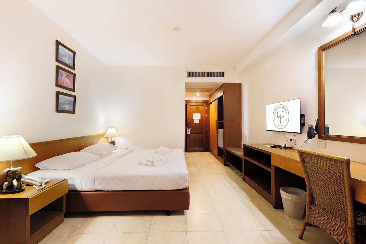 Ein Hotelzimmer mit einem Bett, Nachttischlampen, einem Schreibtisch mit Stuhl, einem Mülleimer und einem an der Wand montierten Fernseher.