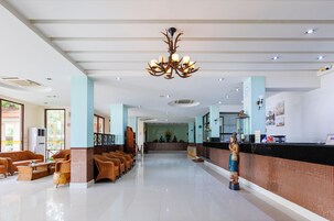 A hotel lobby with a reception desk, wicker furniture, a chandelier, and a statue.