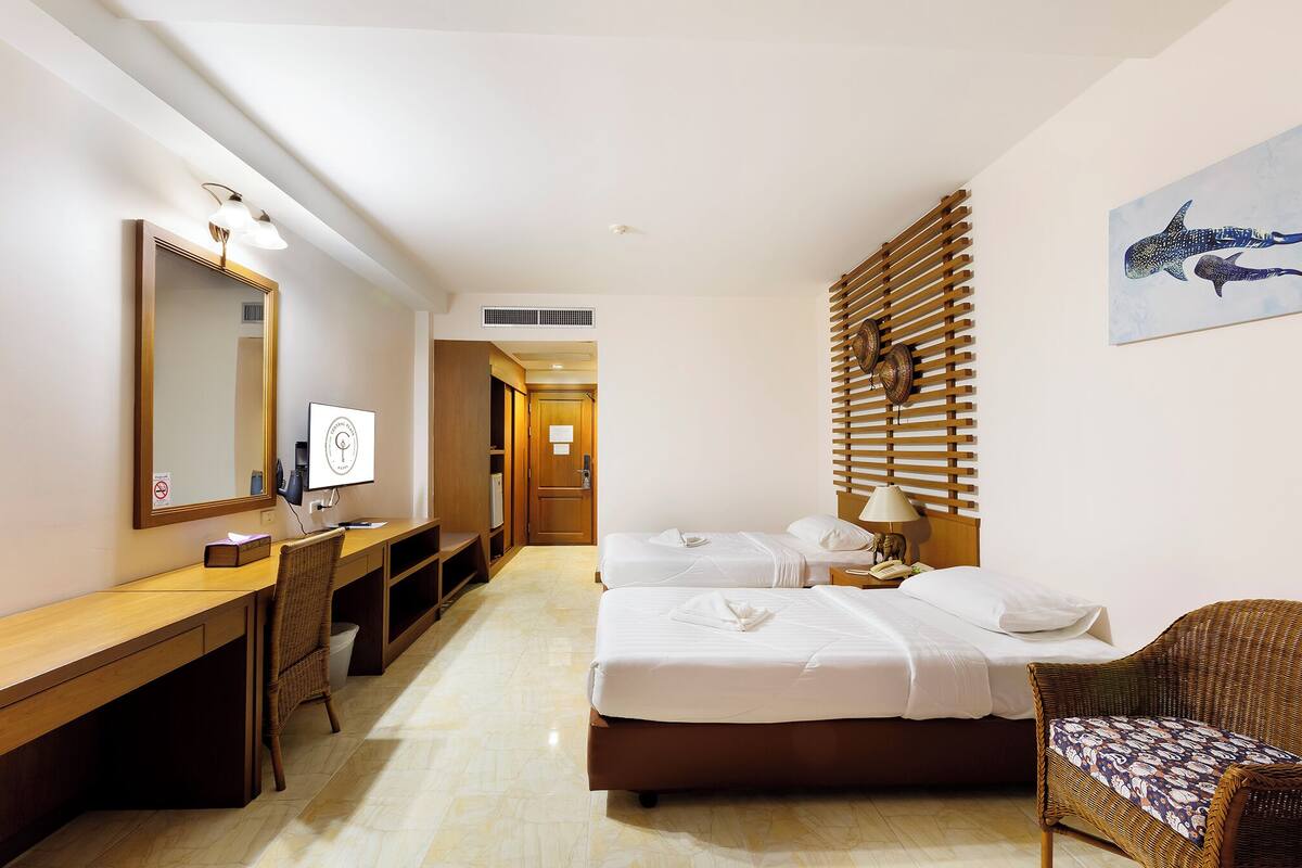 Ein Hotelzimmer mit zwei Betten, einem Schreibtisch mit Stuhl, einem großen Spiegel und einer Wandpaneele aus Holz.