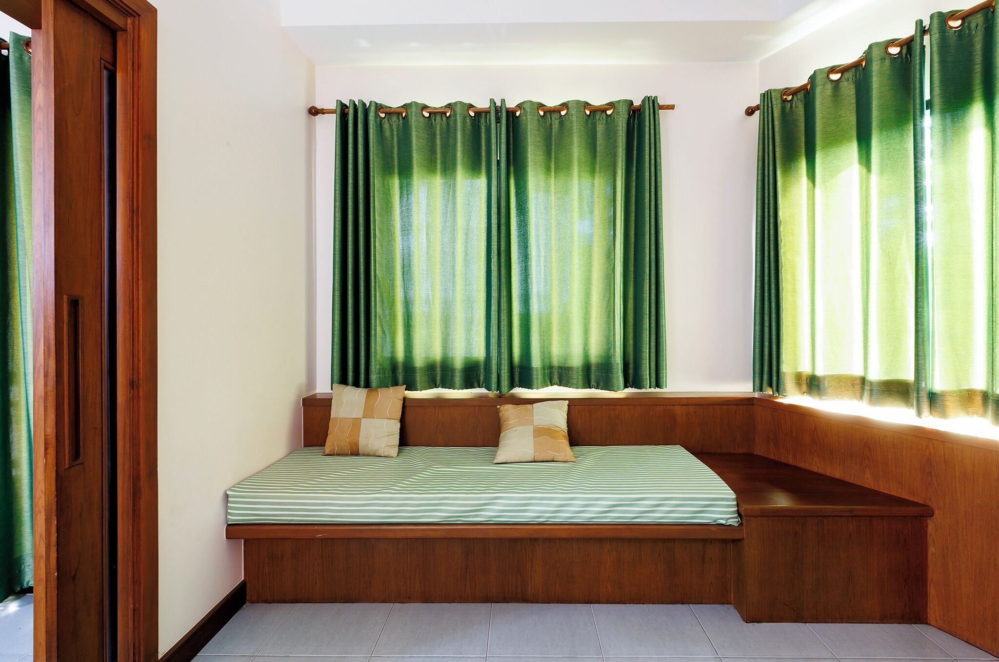 A room with a built-in bench bed, wooden walls, and green curtains.