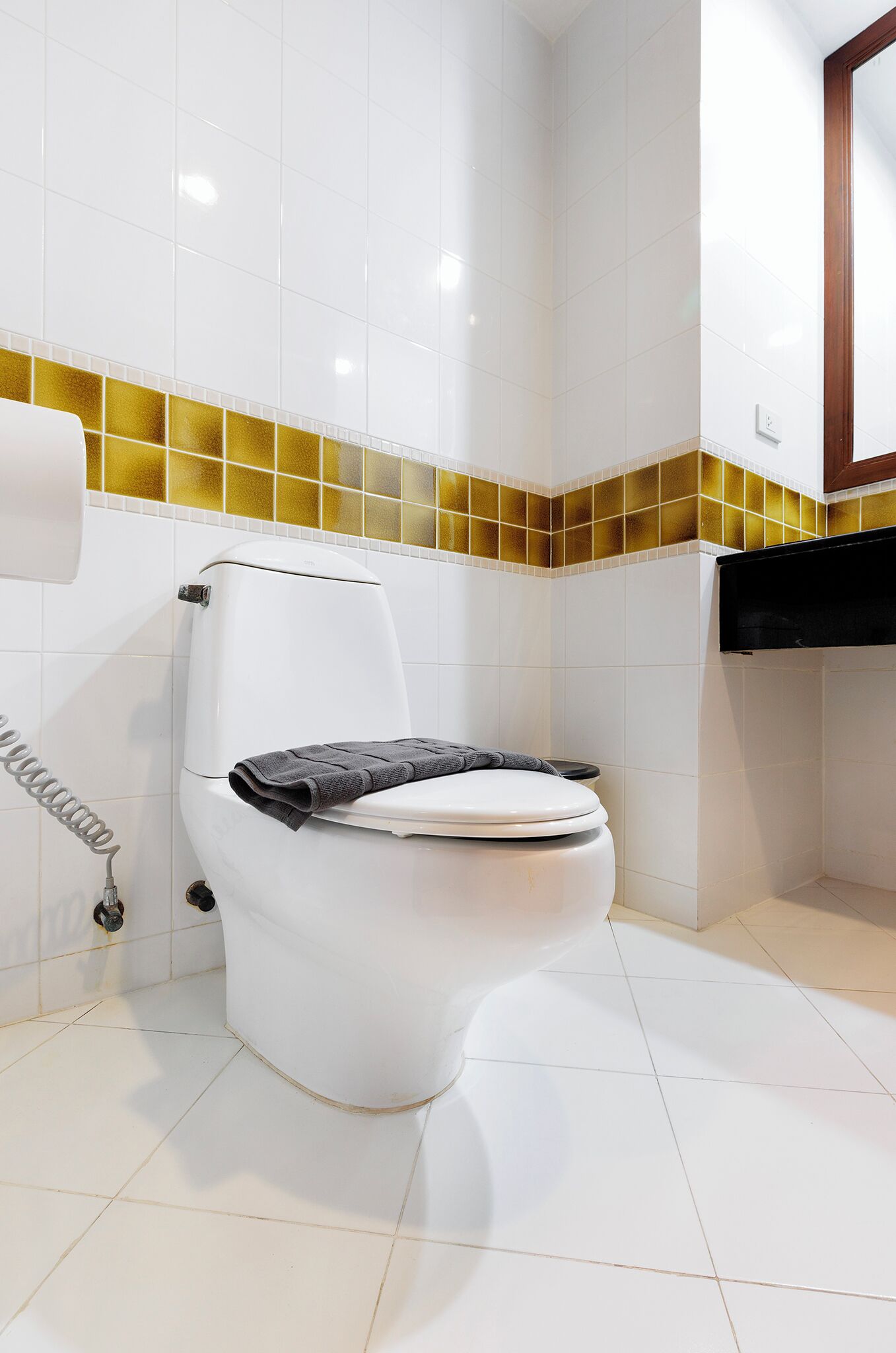 A white toilet with a towel on the seat, a toilet paper holder, and a yellow-tiled backsplash.