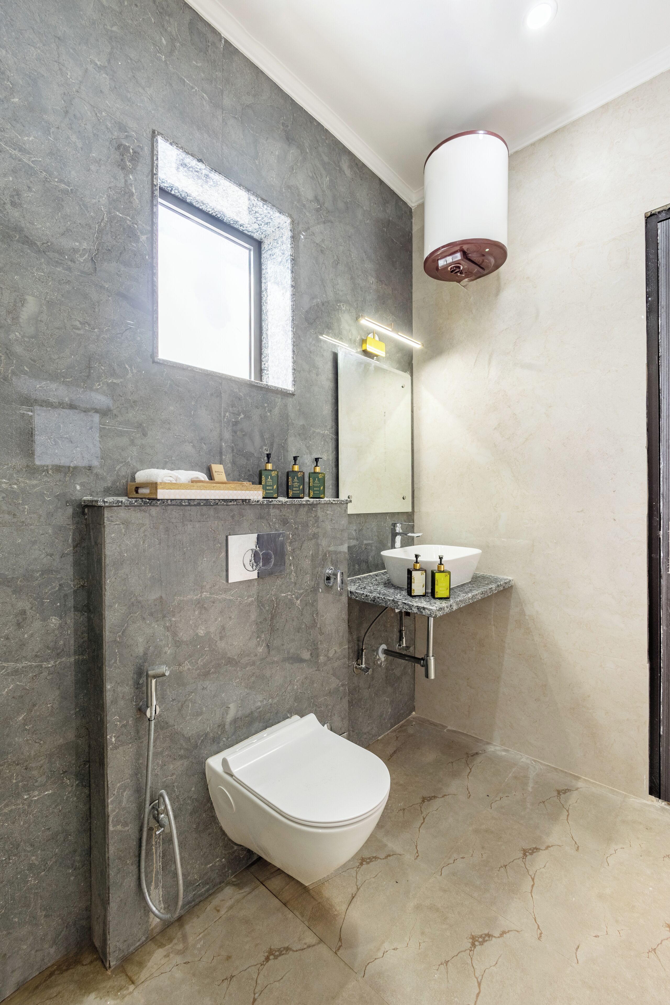Un baño moderno con piso de mármol, un inodoro blanco, un bidé, un lavamanos con espejo y un perchero para toallas.