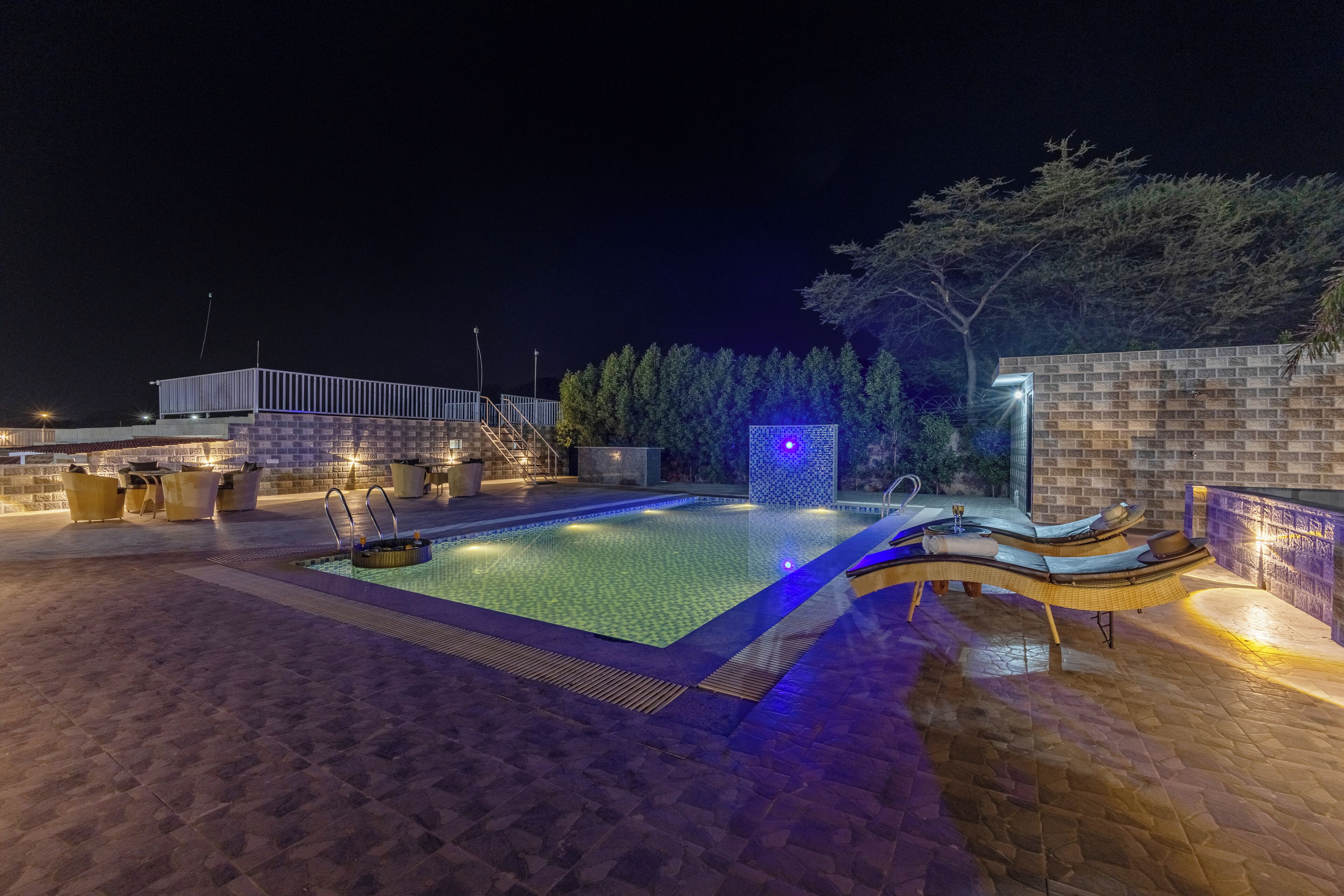 A swimming pool with a tiled deck, lounge chairs, and a stone wall.
