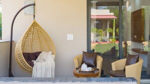 Una habitación con una silla colgante, dos sillones, una mesita con una tetera y un vidrio que da a un espacio exterior.