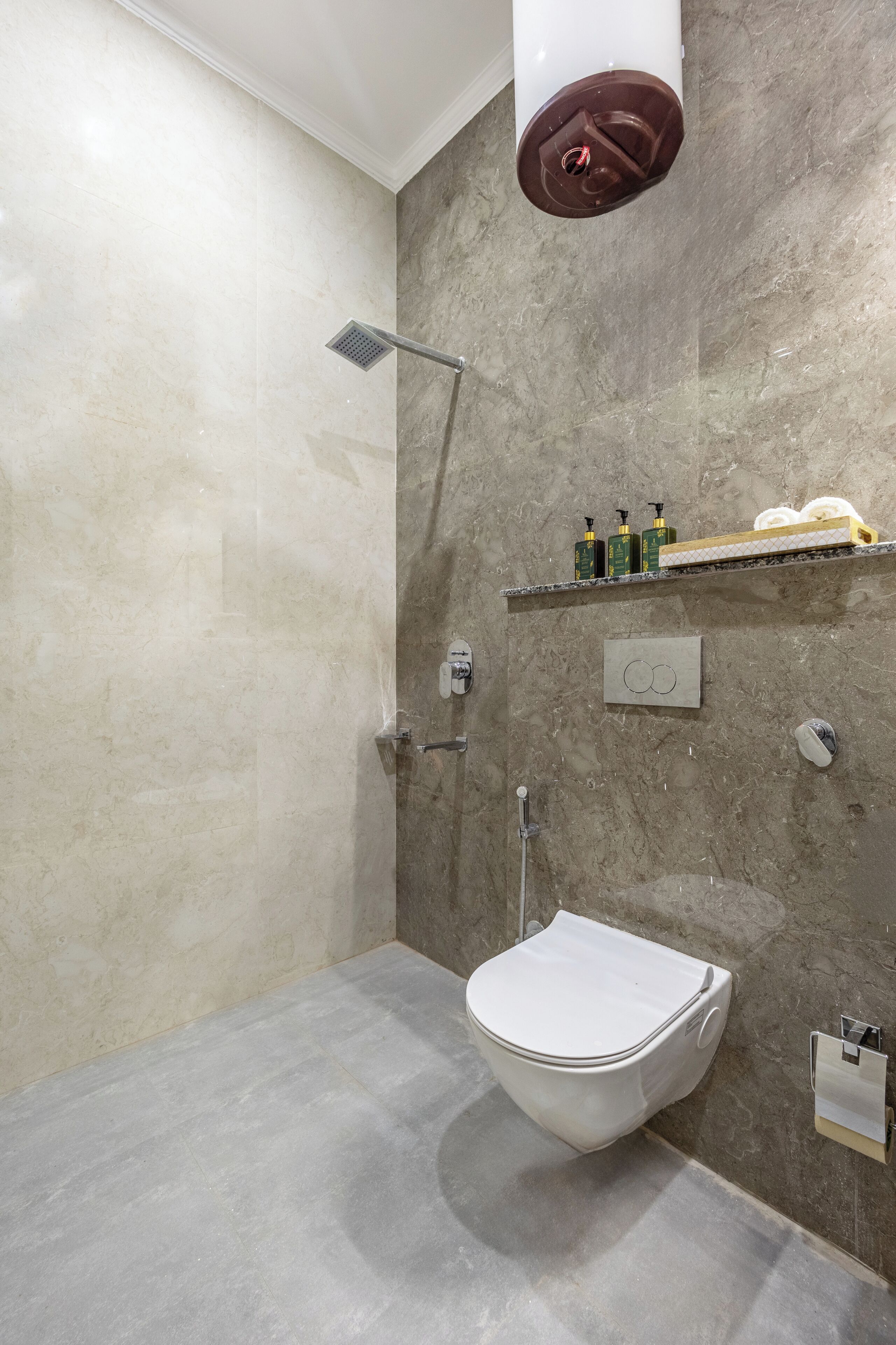 A modern bathroom with a freestanding toilet, a showerhead, and a shelf with toiletries.