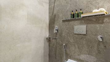 A modern bathroom with a freestanding toilet, a showerhead, and a shelf with toiletries.