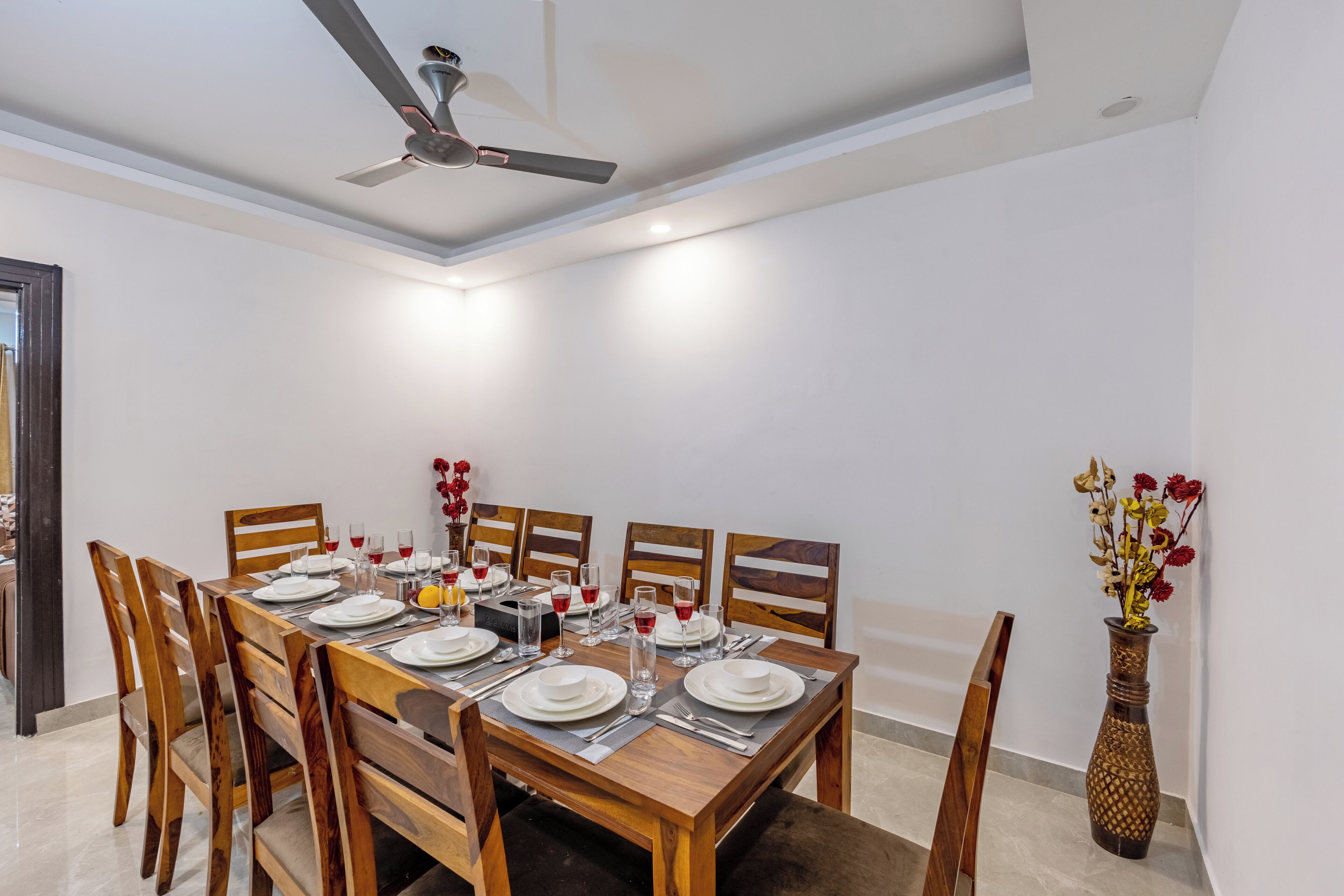 Un comedor con una mesa de madera preparada para seis, sillas, un ventilador de techo y un florero con flores.