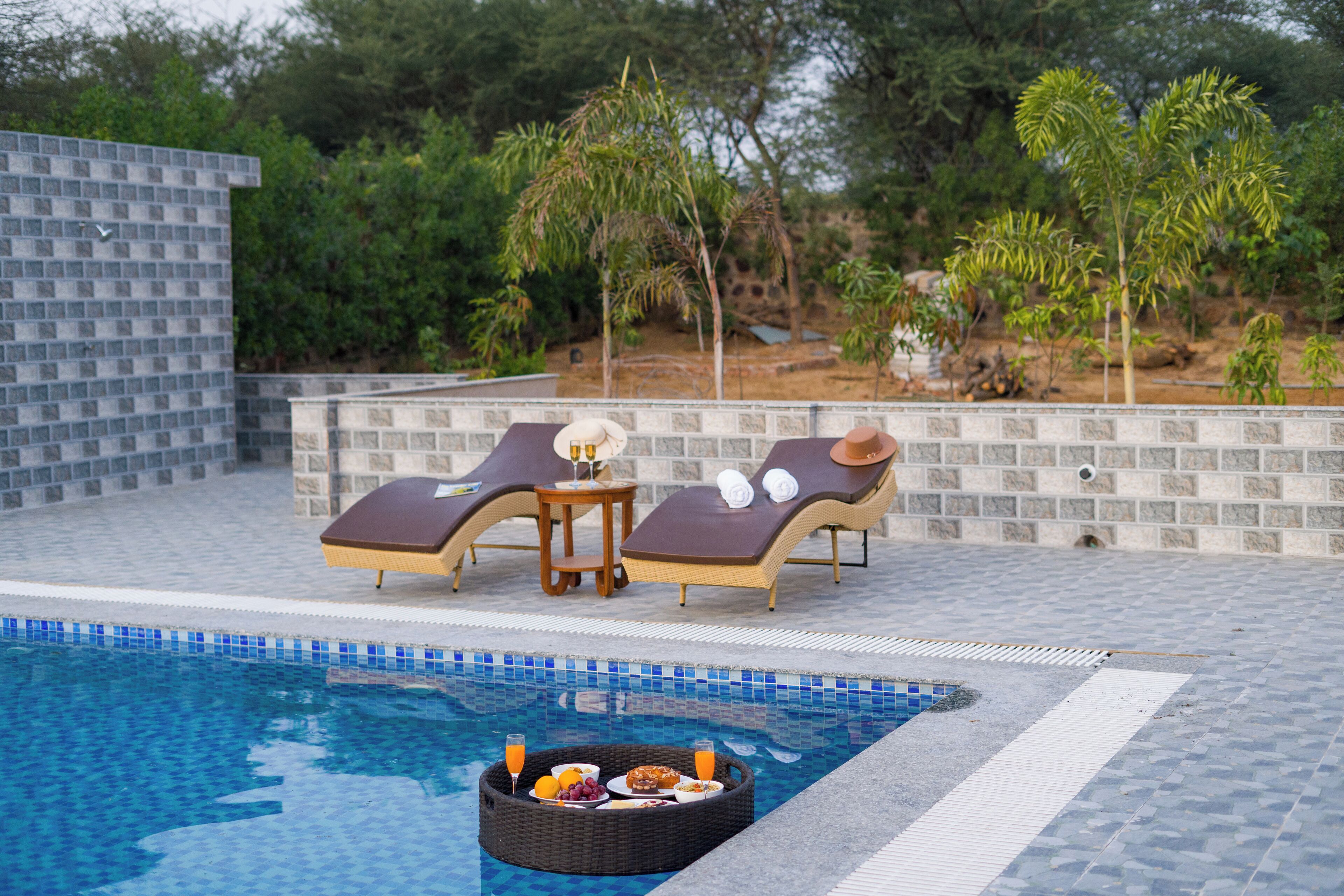 A poolside area with lounge chairs, a small table, and a wicker tray with food and drinks.