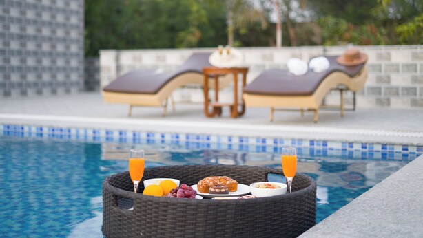 Desayuno junto a la piscina, con una cesta de mimbre que contiene un vaso de zumo de naranja, un vaso de agua, uvas, un muffin y un bol de cereales.