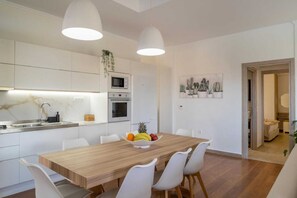 Een moderne keuken met witte kasten, een houten eettafel en een schaal fruit.