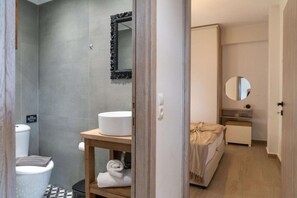 Een moderne badkamer met een douche, toilet en wastafel. Een houten plank met handdoeken en een spiegel boven de wastafel.