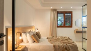 A bedroom with a bed, bedside lamp, window, and a mirror on the wall. - Villa in Kastellákia with Private Pool & BBQ (Rethymno)