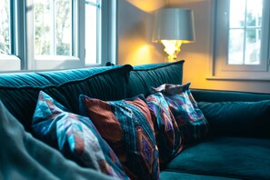 Un canapé de couleur turquoise agrémenté de coussins à motifs, avec une lampe en arrière-plan.
