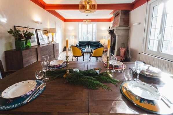 Une salle à manger avec une table en bois dressée pour le repas, une cheminée et une vue sur l’extérieur.