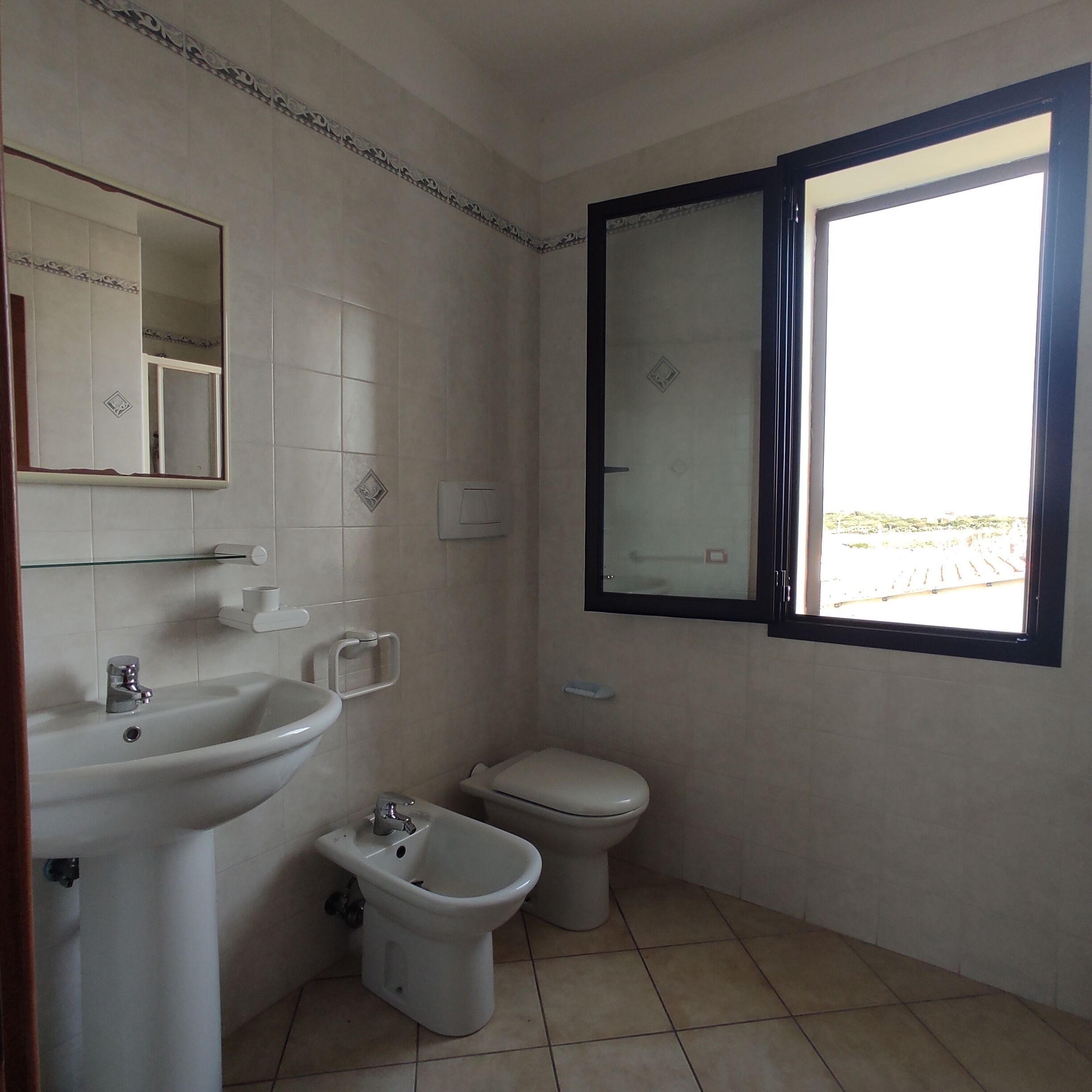 A small, clean bathroom with a sink, bidet, toilet, and a window with a view of the outdoors.