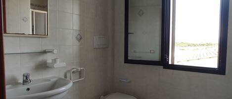 A small, clean bathroom with a sink, bidet, toilet, and a window with a view of the outdoors.