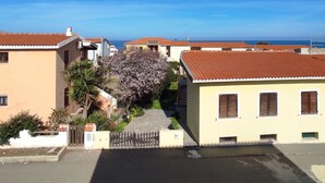 A residential area with houses having red-tiled roofs, a clear blue sky, and a view of the sea in the background. - Residenza Agnese Sardegna (La Ciaccia)