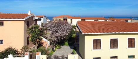 A residential area with houses having red-tiled roofs, a clear blue sky, and a view of the sea in the background.