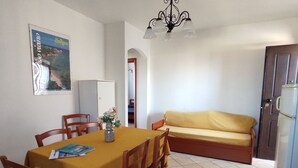 A dining area with a table set for four, a sofa, a refrigerator, and a door leading to another room. - Residenza Agnese Sardegna (La Ciaccia)