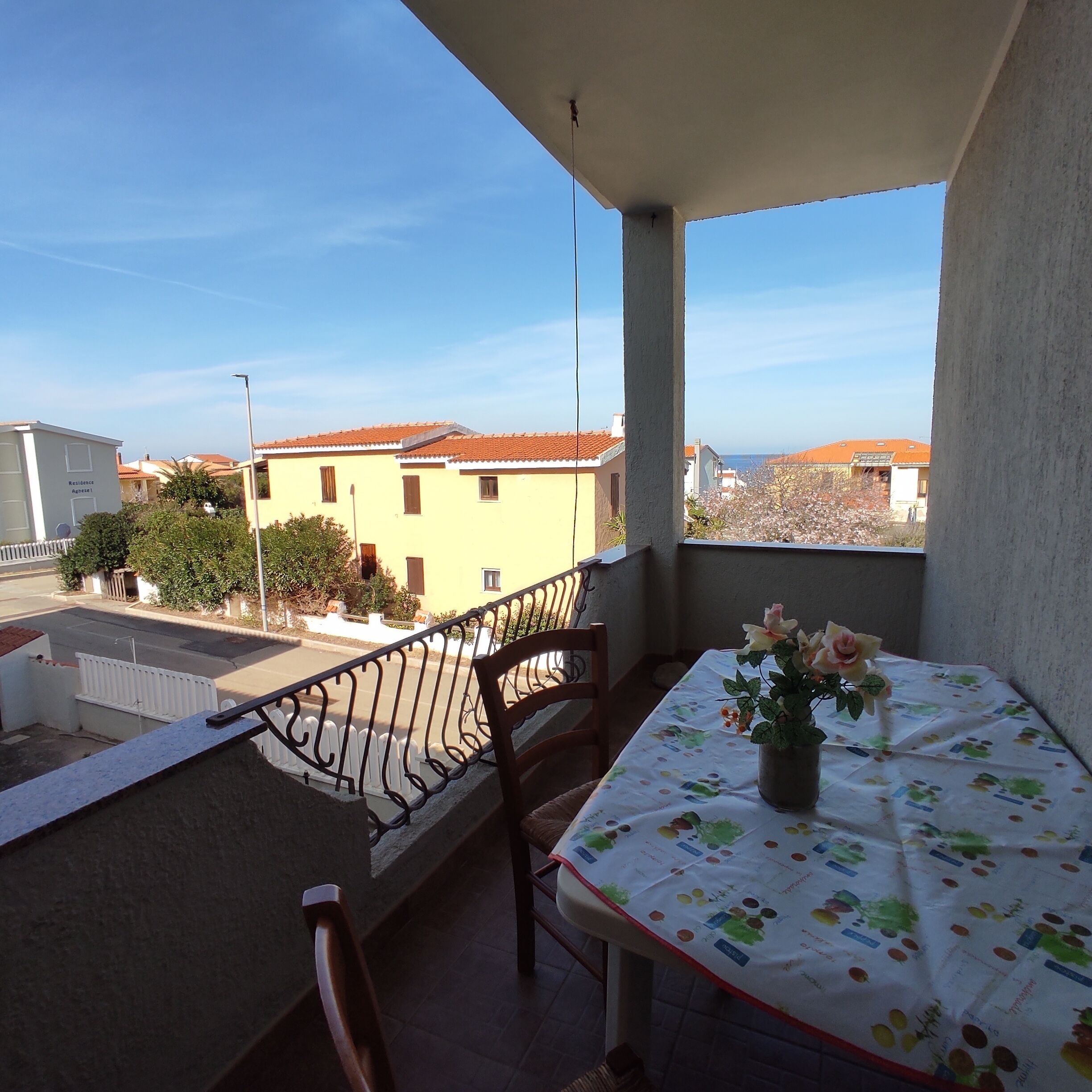 Un balcón con mesa y sillas, vista a edificios y cielo despejado.