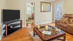 Een woonkamer met een flatscreen televisie, een glazen salontafel, een leren bank en een deur met een glas-in-loodraam.