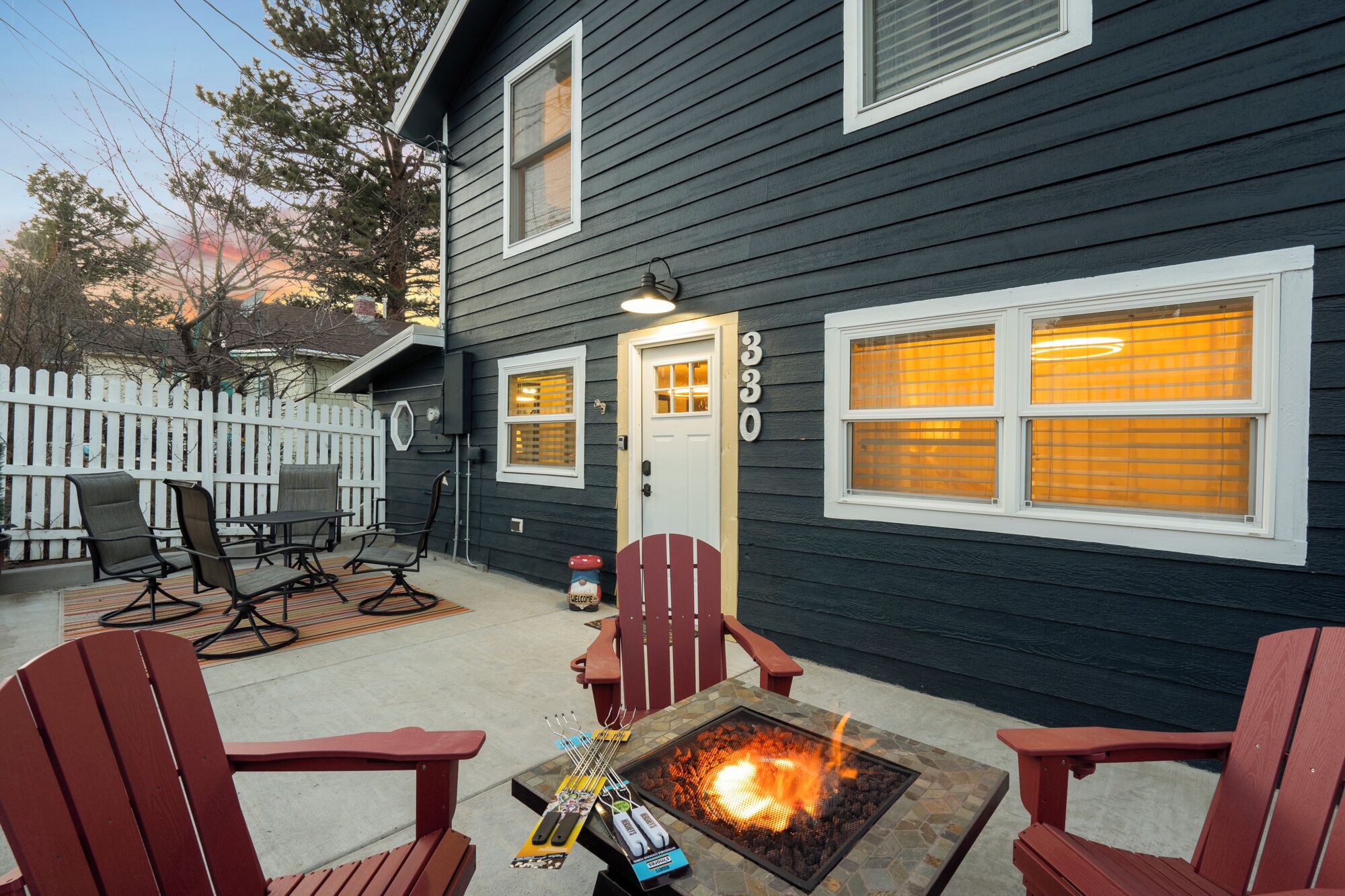 A house with a fire pit in the backyard, outdoor seating, and a white picket fence.
