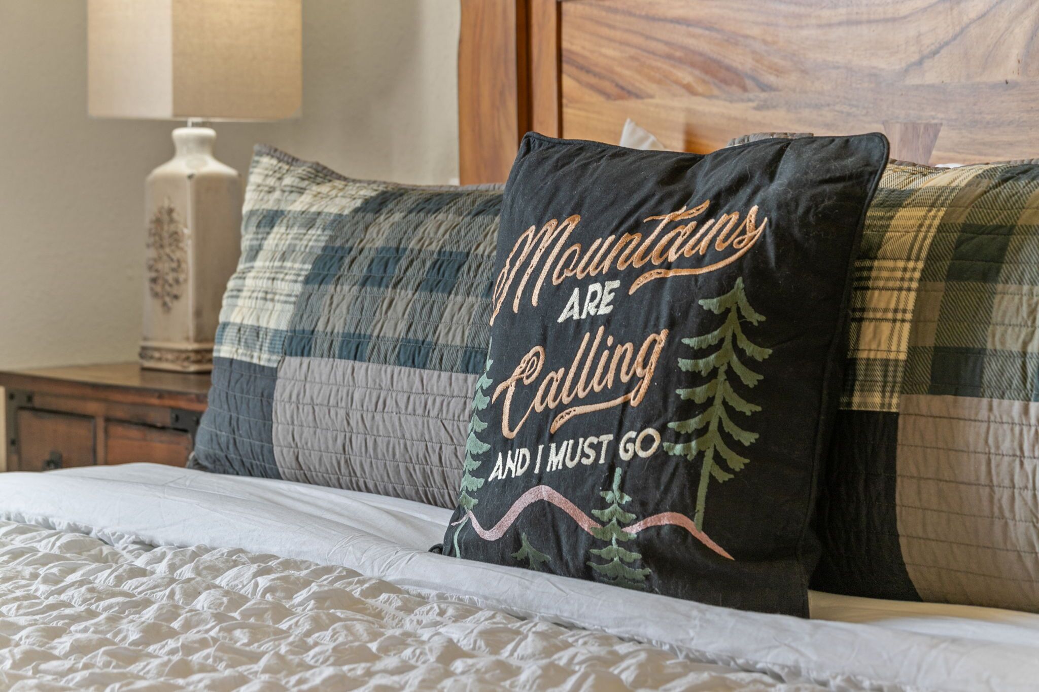 A bed with a white quilted cover and multiple pillows, one with a mountain-themed design.