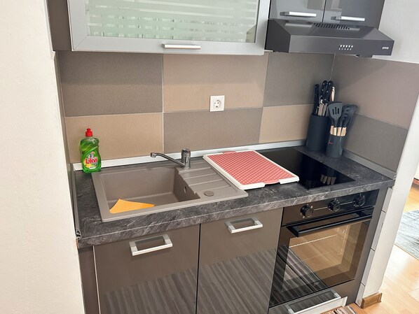 A kitchen with a sink, a red mat, a dish rack, a stove, and a microwave. - Apartman Ana 3 (Dramalj)