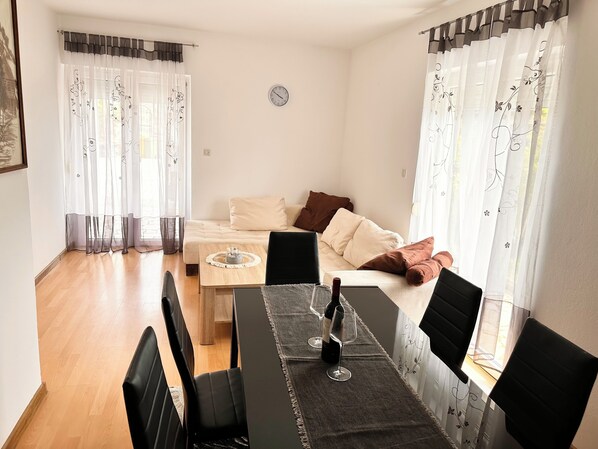 En kompakt opholdsstue med en sofa, et spisebord med stole og et ur på væggen.
